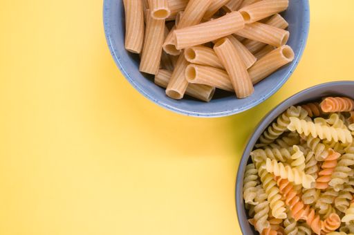A top view of tri-color rotini and rigatoni pasta on a bowl isolated on yellow background