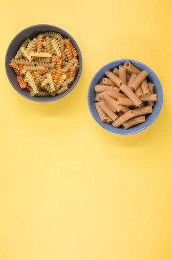 A vertical shot of tri-color rotini and rigatoni pasta on a bowl isolated on yellow background