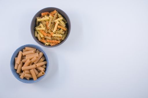 A top view of tri-color rotini and rigatoni pasta on a bowl isolated on white background