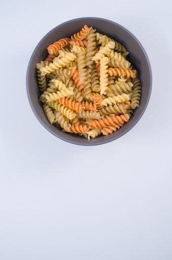 A vertical shot of tri-color rotini pasta on a bowl isolated on white background