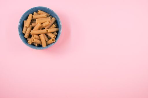 A top view of rigatoni pasta on a bowl isolated on pink background
