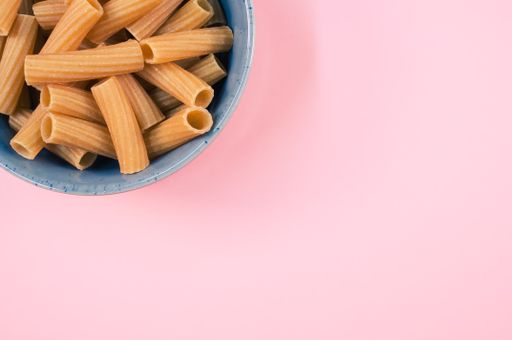 A top view of rigatoni pasta on a bowl isolated on pink background