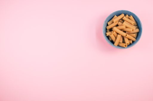 A top view of rigatoni pasta on a bowl isolated on pink background