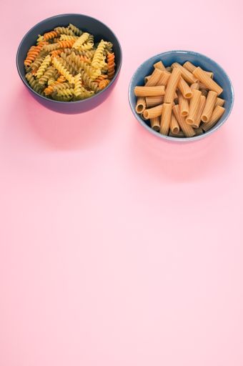 A vertical shot of tri-color rotini and rigatoni pasta on a bowl isolated on pink background