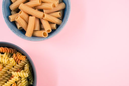 A top view of tri-color rotini and rigatoni pasta on a bowl isolated on pink background