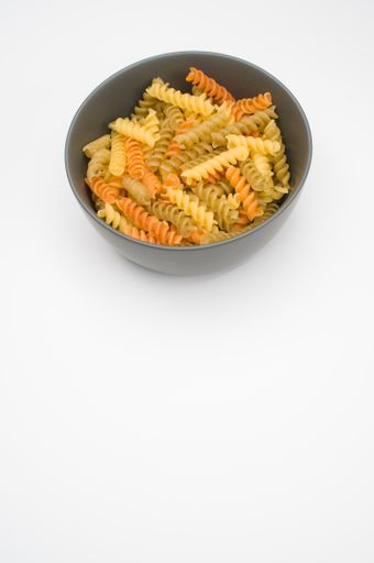 A vertical shot of tri-color rotini pasta on a bowl isolated on white background