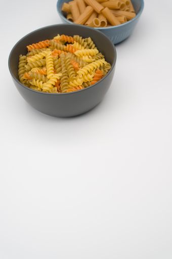 A vertical shot of tri-color rotini and rigatoni pasta on a bowl isolated on white background