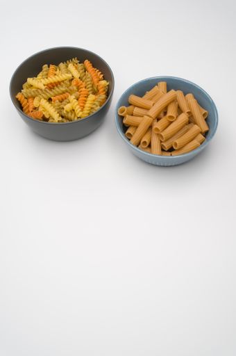 A vertical shot of tri-color rotini and rigatoni pasta on a bowl isolated on white background
