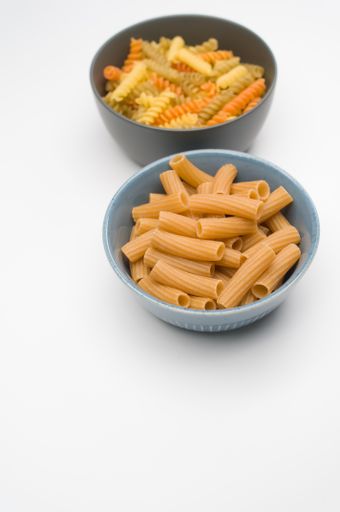 A vertical shot of tri-color rotini and rigatoni pasta on a bowl isolated on white background