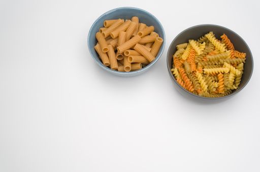 A top view of tri-color rotini and rigatoni pasta on bowls isolated on white background