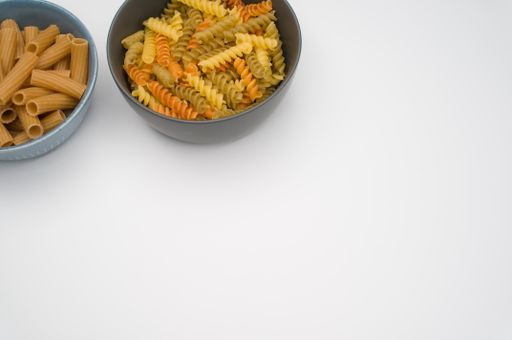 A top view of tri-color rotini and rigatoni pasta on bowls isolated on white background