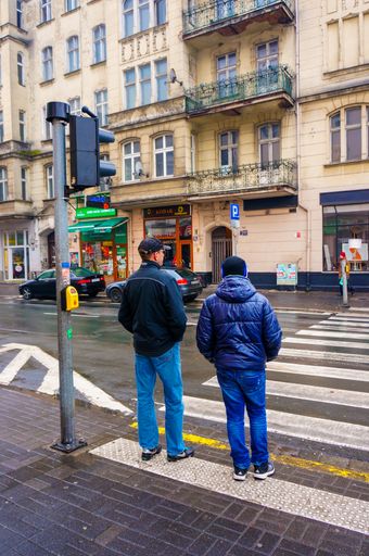 A vertical shot of two males standing in front of a zebra crossing with traffic lights in Poland