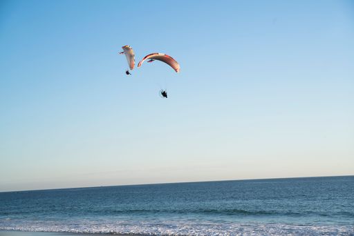Two paragliders soaring over a serene ocean under a clear blue sky, capturing the essence of adventure and freedom.