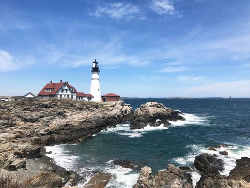 Scenic view of Portland Head Light lighthouse on a rocky coastline under a vibrant blue sky, Cape Elizabeth, Maine.