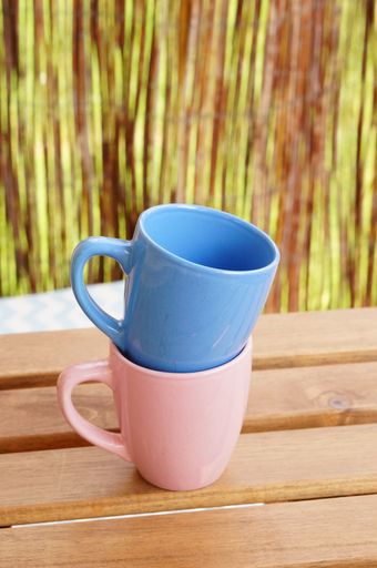 A vertical shot of pink and blue, tea cups in each other on the wooden table with straw background