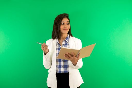 A young businesswoman against a green background, holding a pen and notebook, looking away