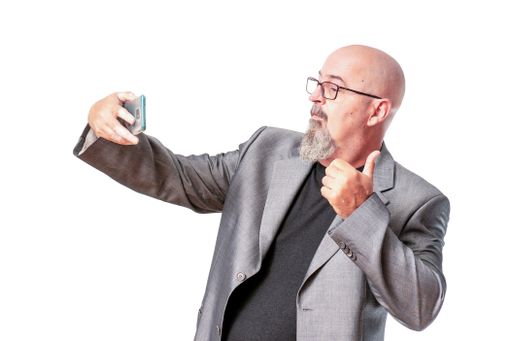 A Caucasian male in an elegant gray suit taking a selfie while standing against an isolated white background