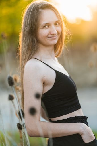 An attractive Caucasian female wearing a black spaghetti strap tank top posing in the meadow at sunset