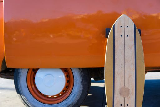 Front view of an Isolated surfskate skateboard leaning on an orange vintage van