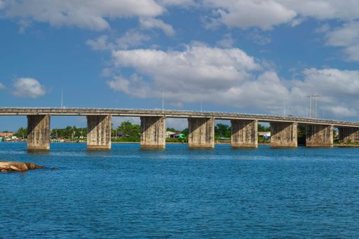 A concrete bridge over blue river with partly cloudy sky in Hua Sai, Thailand