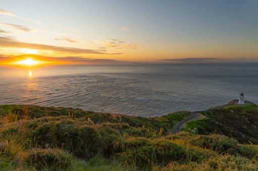 Sunset over Cape Reinga lighthouse with vibrant sky and ocean view in New Zealand.