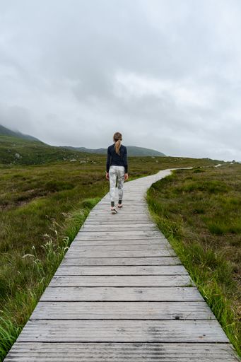 A vertical shot of female walking on wooden footpath on Diamond Hill mountain, Galway Ireland