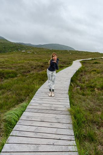 A vertical shot of a female posing on a wooden meadow trail in Ireland