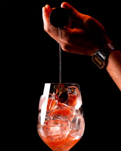 Close-up of a hand pouring liquid into a glass with ice and strawberries against a black background.
