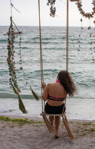 A vertical shot of a female on a swing on the beach enjoying the view of the sea
