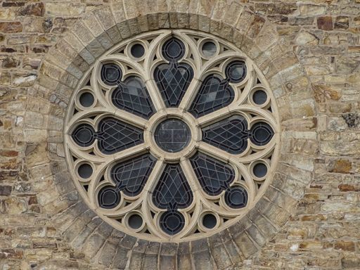 An extravagant gothic style circular window on the brick wall of a medieval monastery
