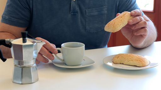 Man enjoying coffee with a stovetop espresso maker and biscuits on a white table.