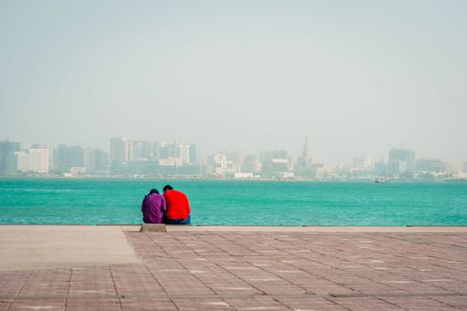 A beautiful shot of a lovely couple sitting near a seashore on the Doha city background, Qatar