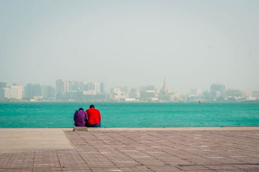 A beautiful shot of a lovely couple sitting near a seashore on the Doha city background, Qatar