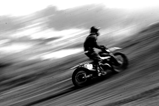 A grayscale shot of a driver on his motorcycle, driving really fas