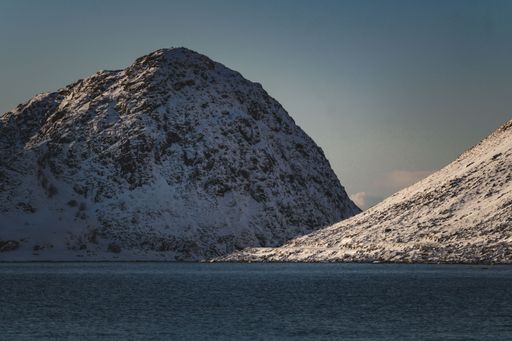 Snow-covered mountains under a clear sky with a tranquil lake in the foreground, showcasing a serene winter landscape.