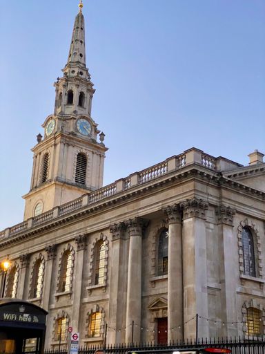 A historic church with a tall clock tower in London against a clear blue sky.