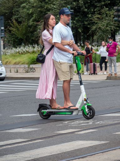A vertical shot of a couple riding on a Lime electric scooter in Milan, Italy