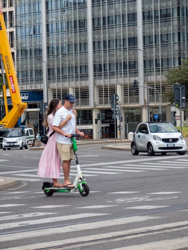 A vertical shot of a couple riding on a Lime electric scooter in Milan, Italy