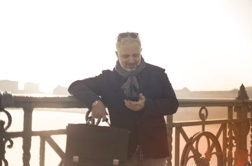A Hungarian man using his phone while leaning on the railings of a bridge at sunset