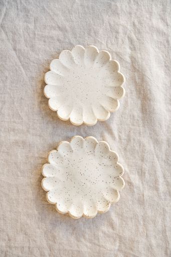 Two speckled ceramic plates with scalloped edges on a textured fabric background.
