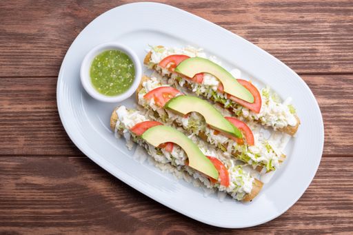A top view of three chicken flautas and a sauce on a white plate