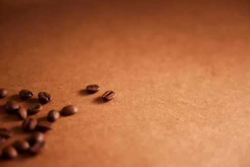 A close-up of few coffee beans scattered on a brown surface, with two isolated beans, creating a warm and minimalist composition