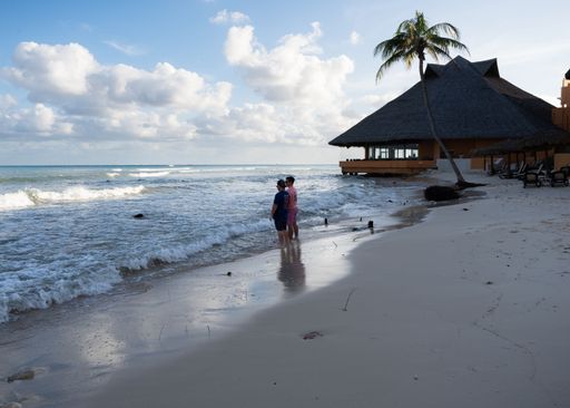 Two young men stand on the beach at sunrise, feet in the sand, enjoying a tropical vacation.