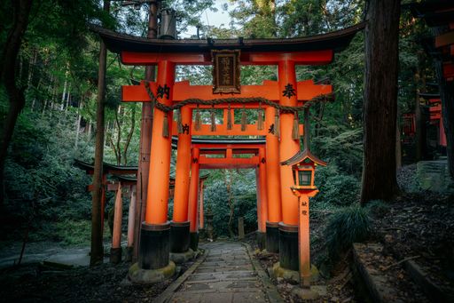 Traditional red torii gates at Fushimi Inari Shrine in Kyoto, Japan, surrounded by lush green forest, creating a serene atmosphere.