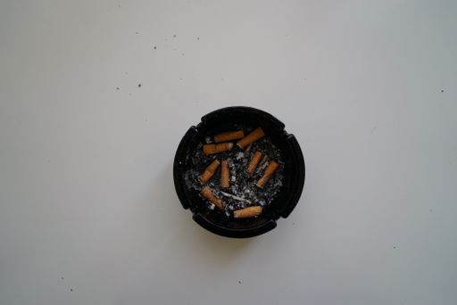 A top view shot of smoked out cigarettes in a black ashtray on a white surface