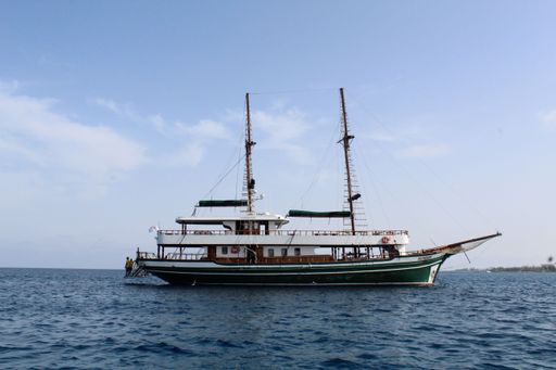 A large sailboat with two masts anchored in calm water under a clear blue sky