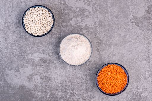 A closeup of three bowls with white beans, flour, and red lentils.
