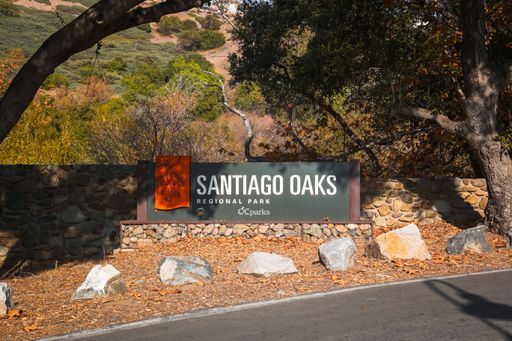A modern sign greets hikers and trail users entering Santiago Oaks Regional Park, a forested green space area in Orange County, California.