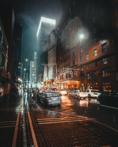 A vertical shot of buildings on a wet street with cars during nighttime