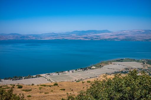 A breathtaking view of the Sea of Galilee in northern Israel, surrounded by farmland and distant hills under a clear blue sky.